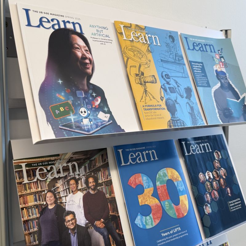 A display rack holding several issues of the 'Learn' magazine, featuring diverse covers related to education and technology. The top magazine highlights 'Anything But Artificial' with a portrait of a woman and digital elements, while the others showcase themes like transformation and educational achievements.